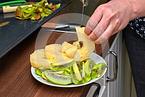 Slicing pineapples and kiwi, a plate of fruit and a hand with a knife