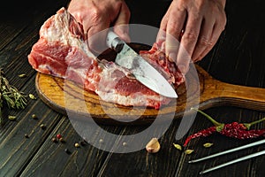 Slicing raw fresh meat with a knife in the hand of a chef. The concept of preparing a meat lunch with spices and rosemary on the