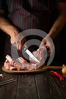 Slicing raw ribs with butcher or cook hands on kitchen cutting board. Barbecue grill. Idea for a restaurant or hotel menu on a