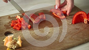 Slicing red bell pepper on wooden cutting board by chef. Female hands is cutting the paprika vegetables. Health eating