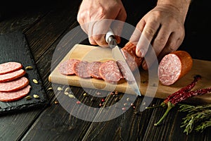 Slicing salami sausage with a knife in the hand of a chef for serving a festive table in a restaurant