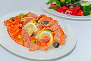 Slicing salmon on a plate close-up selective focus. Cold appetizer of red fish decorated with red caviar, lemon, herbs and olives