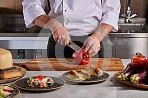 Slicing sweet red pepper on wooden cutting board, cook in uniform preparing salad