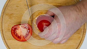 Slicing tomato. Male hands cut a red ripe tomato into small pieces with a sharp knife