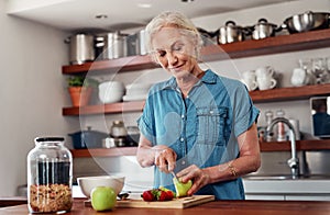 Slicing up her ingredients. an attractive senior woman chopping up apples and other fruit while preparing breakfast in