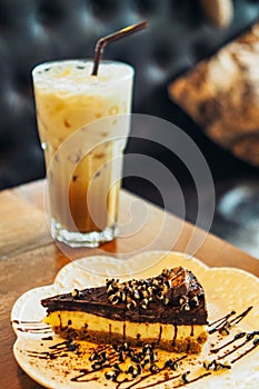 A slide of chocolate cake with iced latte coffee in a  tall glass. cold summer drink background