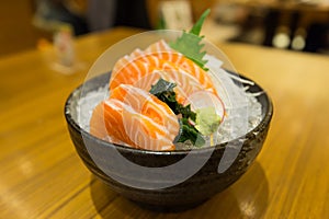 Slide salmon sashimi on ice in black bowl.