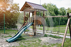 Slide and swings with a wooden house on children playground. Outdoors games for kids