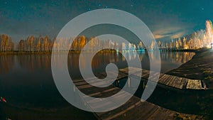 Slider shot of Deep Night Stars Above Lake. Natural Starry Sky Landscape. Wooden Pier. Autumn Forest woods lake