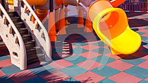 Slides with playground climbing equipment on colorful checkered rubber floor in outdoors playground area at kindergarten
