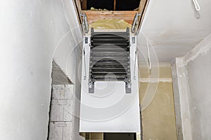 Sliding metal stairs to the attic in the ceiling, an open hatch and compound stairs, modern look.