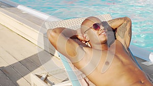 Sliding shot of a handsome African man sunbathing by the pool