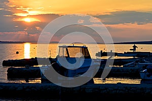 Slightly cloudy sunset above Vrsi Mulo beach with line of molos, boats and silhouette of fisherman visible photo