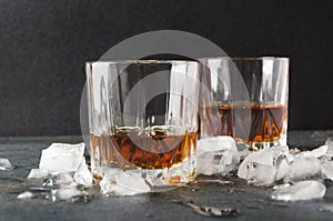 Slightly hot brendy in glasses and ice cubes on gray surface against dark background