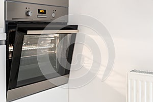 Slightly opened steel oven in white kitchen interior