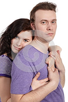 Slightly smiling woman embraces man from behind