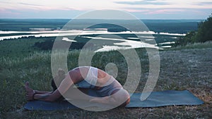 Slim adult woman doing yoga on the hill - stretching down to her leg