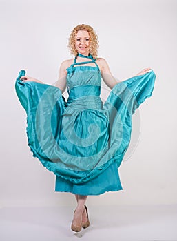 Slim airy girl in flying blue evening dress on white background in Studio