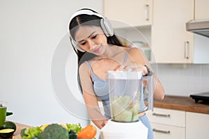 A slim Asian woman in gym clothes is making her healthy green smoothie juice in the kitchen