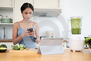 A slim Asian woman is using her smartphone while making her healthy breakfast in the kitchen