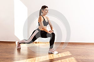 Slim athletic beautiful female stretching legs before workout, lower body exercise.