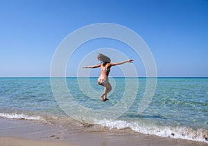 Slim and athletic girl in a bikini at the beach jumping into the air with joy