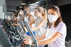 Slim athletic people in protective masks running on treadmill in fitness club