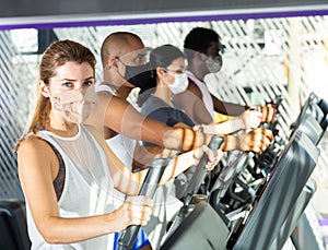 Slim athletic people in protective masks running on treadmill in fitness club