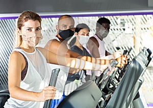 Slim athletic people in protective masks running on treadmill in fitness club