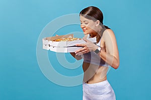 Slim athletic woman in white sportswear enjoying aroma holding in hands box with pizza, avoiding junk food, keeping diet, healthy