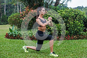 Slim athletic woman working out in park doing knee-bounce exercise or lunges.