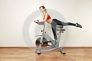 Slim attractive woman standing on exercise bike with raised leg, cardio workout.