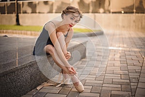 Slim ballerina in a blackdress putting on pointe shoes. outdoor photo