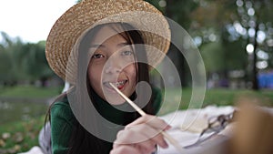 Slim beautiful woman with painting brush posing in summer park at easel. Portrait of happy talented confident Asian