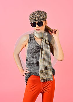 Slim blond model in tartan cap and scarf wearing big black sunglasses isolated on pink background