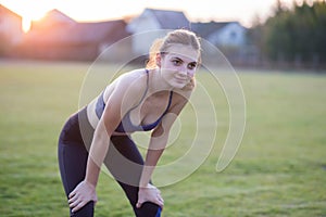 Slim blonde girl plays sports and performs yoga poses in summer grass covered stadium on a sunset background. Woman doing