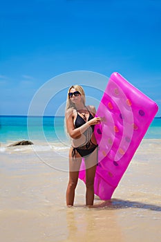 Slim blonde woman with pink swimming mattress on tropical beach
