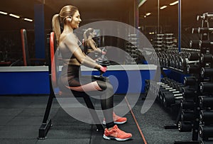 Slim, bodybuilder girl, lifts heavy dumbbell standing in front of the mirror while training in the gym.