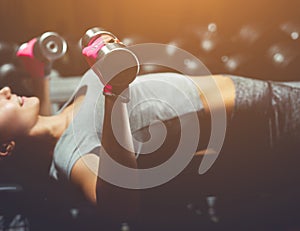 Slim, bodybuilder girl, lifts heavy dumbbell standing in front of the mirror while training in the gym.