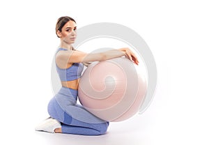 Slim, bodybuilder girl in a lilac tracksuit, sitting on a mat with a Pilates ball, cardio workout. Sports concept, fat burning