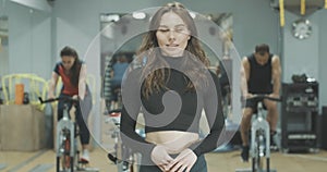 Slim brunette beautiful woman standing in gym and smiling at camera. Portrait of young confident Caucasian girl posing