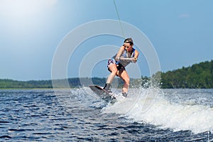 Slim brunette woman riding wakeboard on motorboat wave in lake