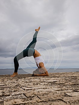 Slim Caucasian woman practicing gymnastic exercise. Wheel pose one leg up. Fitness, wellness concept. Flexible body. Outdoor