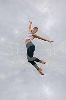 Slim Caucasian young woman jumping over cloudy sky. Caucasian woman wearing sportswear. Fitness, sport, wellness concept. Outdoor