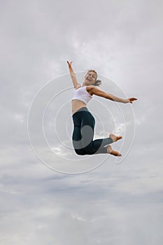 Slim Caucasian young woman jumping over cloudy sky. Caucasian woman wearing sportswear. Fitness, sport, wellness concept. Outdoor