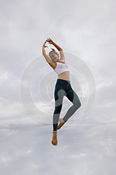 Slim Caucasian young woman jumping over cloudy sky. Caucasian woman wearing sportswear. Fitness, sport, wellness concept. Outdoor