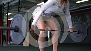 Slim concentrated sportswoman lifting barbell in slow motion squatting in gym. Focused motivated Caucasian fit woman
