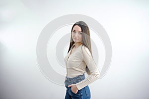 slim cute young girl in jeans on a white background in the studio Attractive brunette put her hands in her back pockets