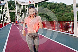 Slim european woman running at stadium with happy face expression. Blithesome girl in gray pants ho