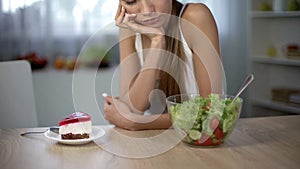 Slim female choosing between cake and salad, healthy diet vs high-calorie food